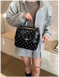 Close-up of black polka dot handbag with silver twist lock and metal chain strap