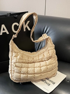 Sac fourre-tout matelassé beige minimaliste avec bandoulière sur un canapé en cuir noir