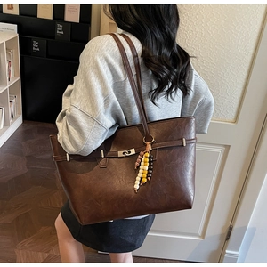 Detail of dark brown faux leather tote bag with silver buckle and colorful beaded charm