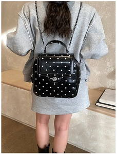 Close-up of black and white polka dot backpack with silver clasp and chain strap