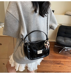 Détail du sac à bandoulière plissé noir brillant avec pendentif poupée et chaîne de perles