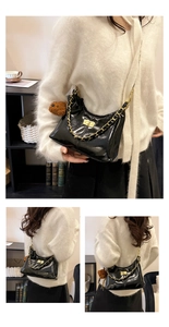 Detail der glänzenden schwarzen Leder-Hobo-Tasche mit goldener Kette und Bärenanhänger