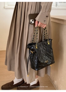 Détail d'un sac seau noir matelassé avec une chaîne dorée et le logo frontal