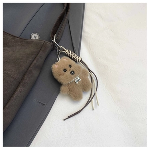 Detail of a plush brown puppy bag charm with a bone tag on a leather handbag