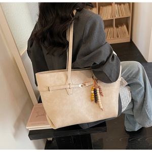 Detail of cream beige tote bag with metallic buckle and colorful beaded tassel detail