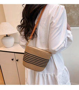 Detail of hand-woven straw bucket bag with black stripes and brown leather strap