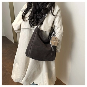 Detail of a large brown hobo bag with a plush bear charm on a trench coat model