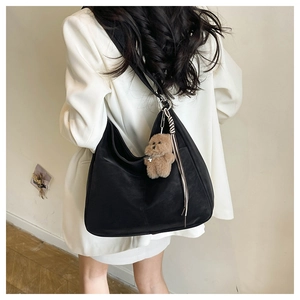 Close-up of black half-moon hobo bag with cute bear charm and tassel on white blazer