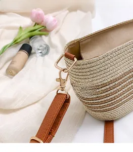Close-up of golden metal lobster clasp and brown leather strap on a straw bucket bag