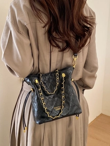 Sac à bandoulière noir matelassé avec chaîne dorée porté par un mannequin dans un décor épuré