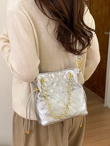 Sac seau matelassé argenté avec chaîne dorée porté par un mannequin en intérieur