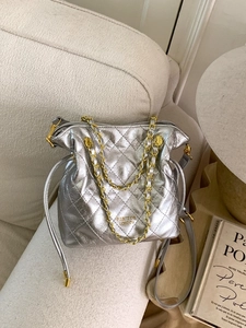 Sac seau matelassé argenté avec chaîne dorée sur une chaise blanche, style vintage