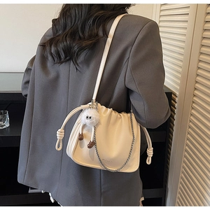Detail of beige pleated bucket bag with metal chain, strap and fluffy eye charm accessory