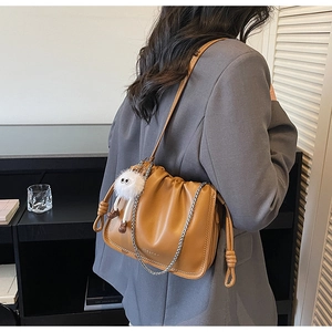 Detail view of caramel pleated bucket bag with metal chain strap and plush keychain