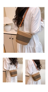 Detail of woven straw bucket bag featuring black stripes and adjustable leather strap