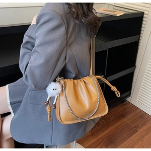 Detail of a ginger leather pleated bucket bag with silver chain and plush pendant
