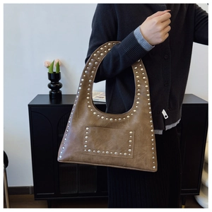 Close-up of vintage brown tote bag featuring silver rivet studs and a wide shoulder strap