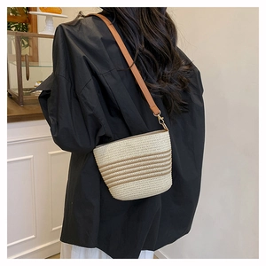 Detail of striped straw bucket bag with brown leather strap against black shirt background