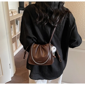 Detail of a dark brown pleated cloud bucket bag with a plush charm and silver chain