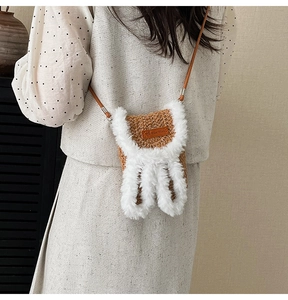 Detailed view of brown woven crossbody bag with white plush bunny ears and leather strap