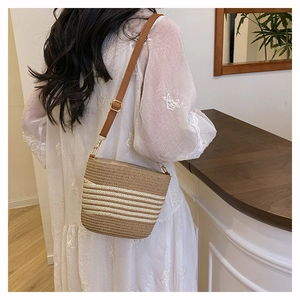 Detail view of woven straw bucket bag with white stripes and brown crossbody strap