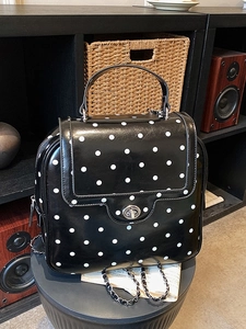 Polished black polka dot backpack with silver chain strap and top handle in studio setting