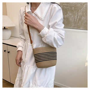 Detailed close-up of a woven straw bucket bag featuring black stripes and a leather strap