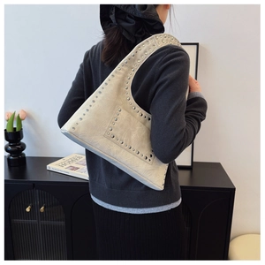 Detail of beige oil wax leather shoulder bag with silver rivets worn in modern interior