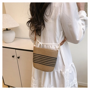 Detail of straw bucket bag with black stripes and brown adjustable leather strap