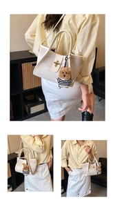 Detail of off-white canvas tote bag with golden twist lock and bear charm accessory