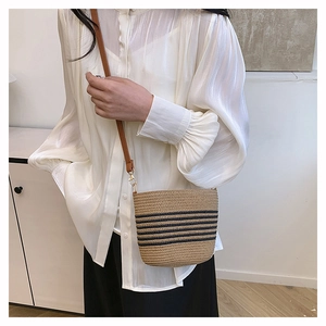 Detail of handwoven straw bucket bag with blue stripes and leather strap on model