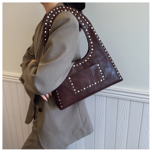 Detailed shot of dark brown rivet studded shoulder bag styled on a grey blazer