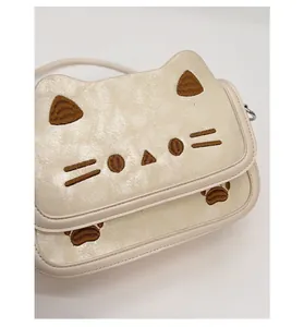 Detail view of the embroidered cat face and PU leather texture on beige crossbody bag