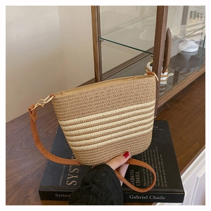 Detail of striped straw bucket bag featuring a brown leather strap and gold hardware