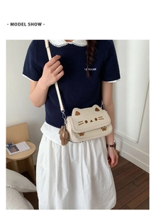 Detail of cream kitten-shaped crossbody bag featuring cat ear embroidery and plush bear charm