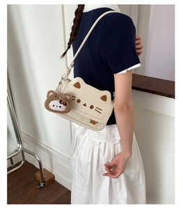 Detail of cream cat-shaped handbag featuring brown embroidery and a plush bear charm