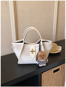 Detail view of cream canvas tote bag with gold twist lock and cute plush puppy charm