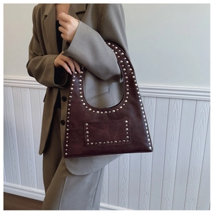 Detailed close-up of dark brown vintage leather shoulder bag with silver metal rivets