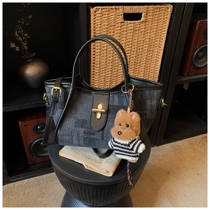 Detail of dark grey denim tote with black leather trim and cute teddy bear charm accessory