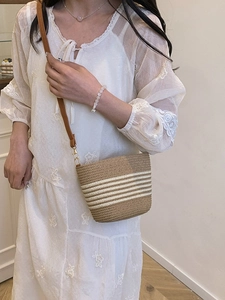 Straw bucket bag with beige stripes and brown leather strap for summer beach vacations