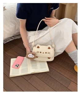 Close-up of cream PU leather cat-shaped crossbody bag with a plush bear charm