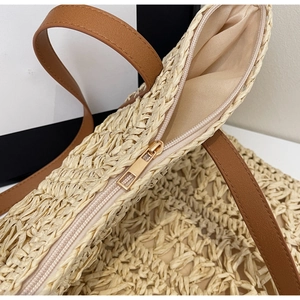 Close-up of the woven texture, top zipper closure, and brown leather handles of the tote bag