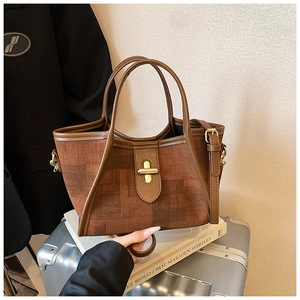 Detail of a brown fabric bucket bag with gold metal buckle on a silver suitcase