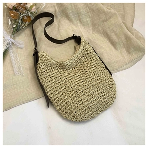 Detail of hand-woven beige straw tote bag with brown leather strap on textured fabric