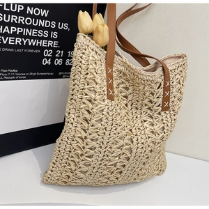 Close-up of woven straw tote bag with brown leather straps and cross-stitch details