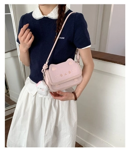 Close-up of pink cat-shaped crossbody bag with embroidered facial details and plush charm