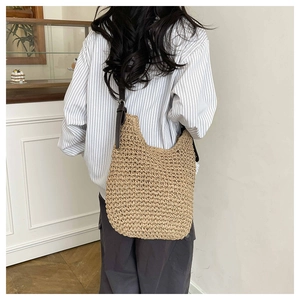 Detail of woven straw tote bag featuring a brown leather strap and metal buckle