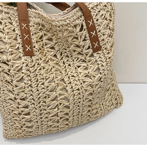 Detailed view of woven straw tote bag with brown faux leather handles and white cross stitching