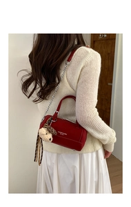 Close-up of red cylindrical crossbody bag with metal chain strap and teddy bear charm