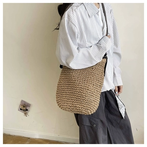 Close-up of natural woven straw tote bag with brown leather shoulder strap in detail
